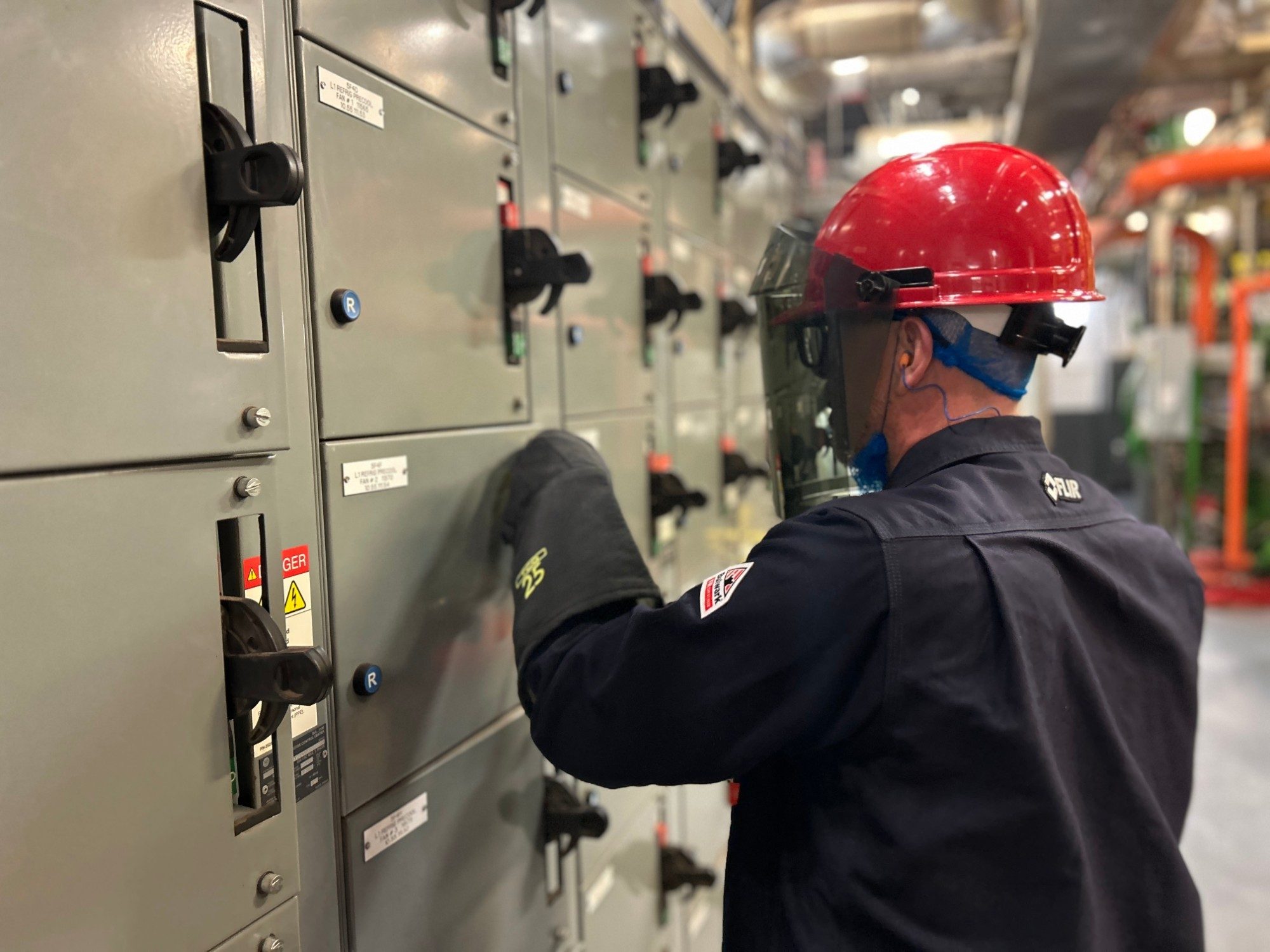 Technician in an arc-rated face shield and gloves at a motor control centre